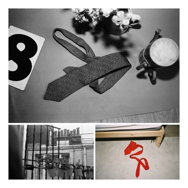 Still life in monochrome featuring a tie, card with the number eight, flowers in a vase, and a small pot on a colored surface.