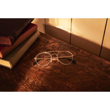 Pair of gold-rimmed glasses on a rustic wooden table with stacked antique books, creating a warm, vintage aesthetic.