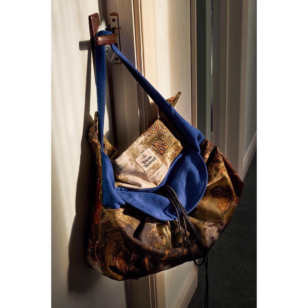Designer handbag with artwork hanging from a door, featuring a blue interior, patterned exterior, and a logo patch, indoor setting.