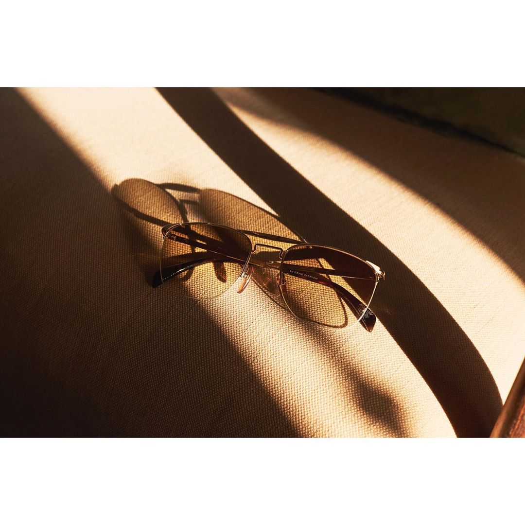 Close-up of modern metal-framed sunglasses with amber lenses on tan fabric surface with sharp shadows, conveying contemporary style.