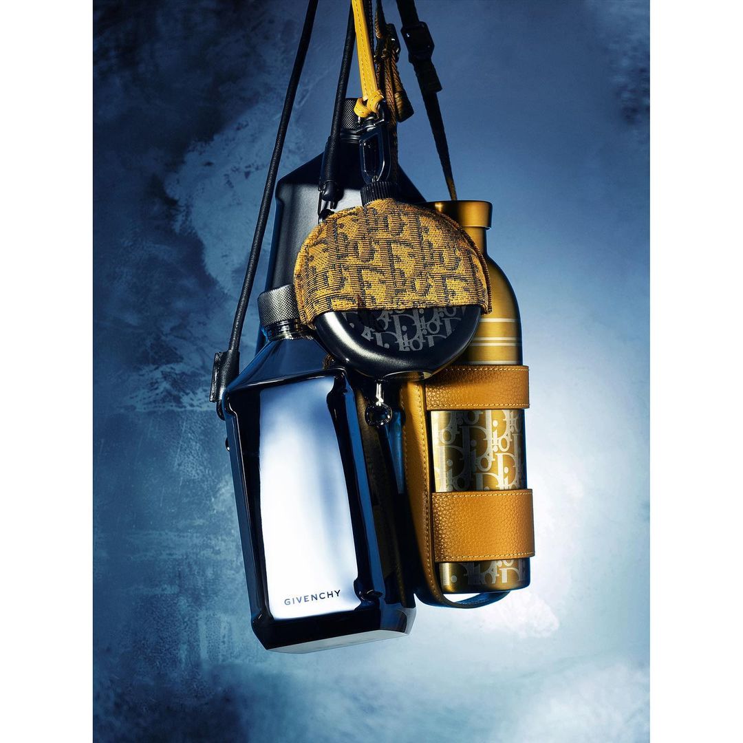 Still life shot of Givenchy and Dior water bottles and accessories. Dark blue background with light highlights and studio lighting.