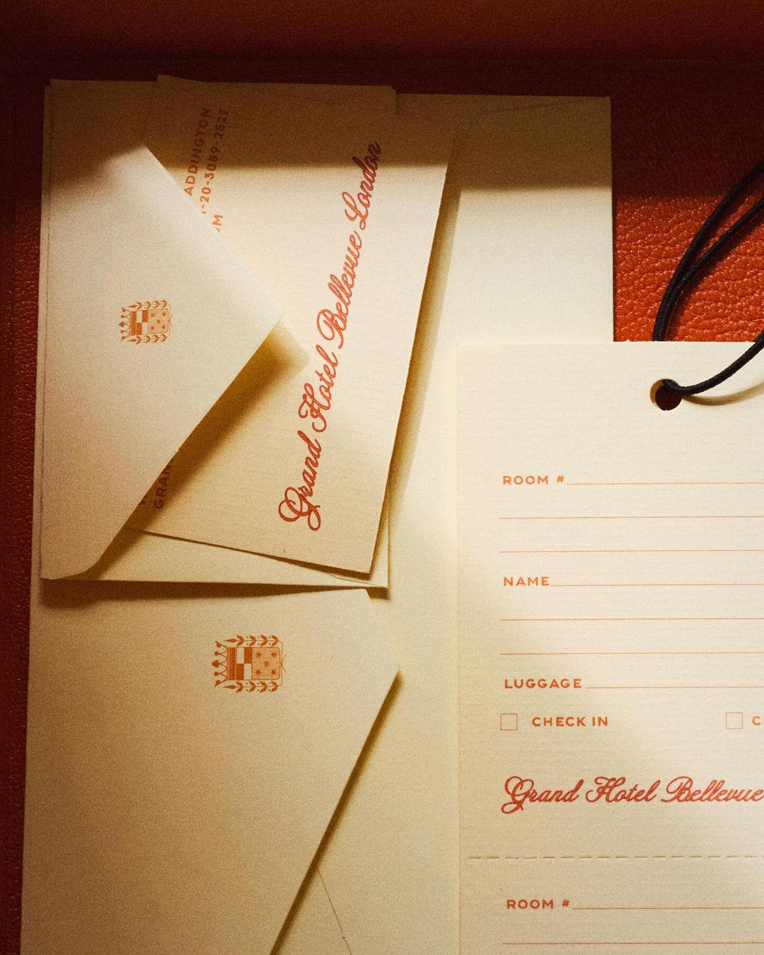 Stationery set features envelopes and a luggage tag from the Grand Hotel Bellevue London, displayed against an orange textured background.