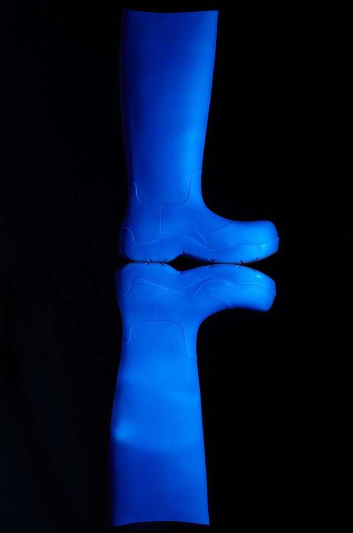 A bright blue rubber boot is isolated on a black reflective surface in a product-style shot showing the design and texture of the material.