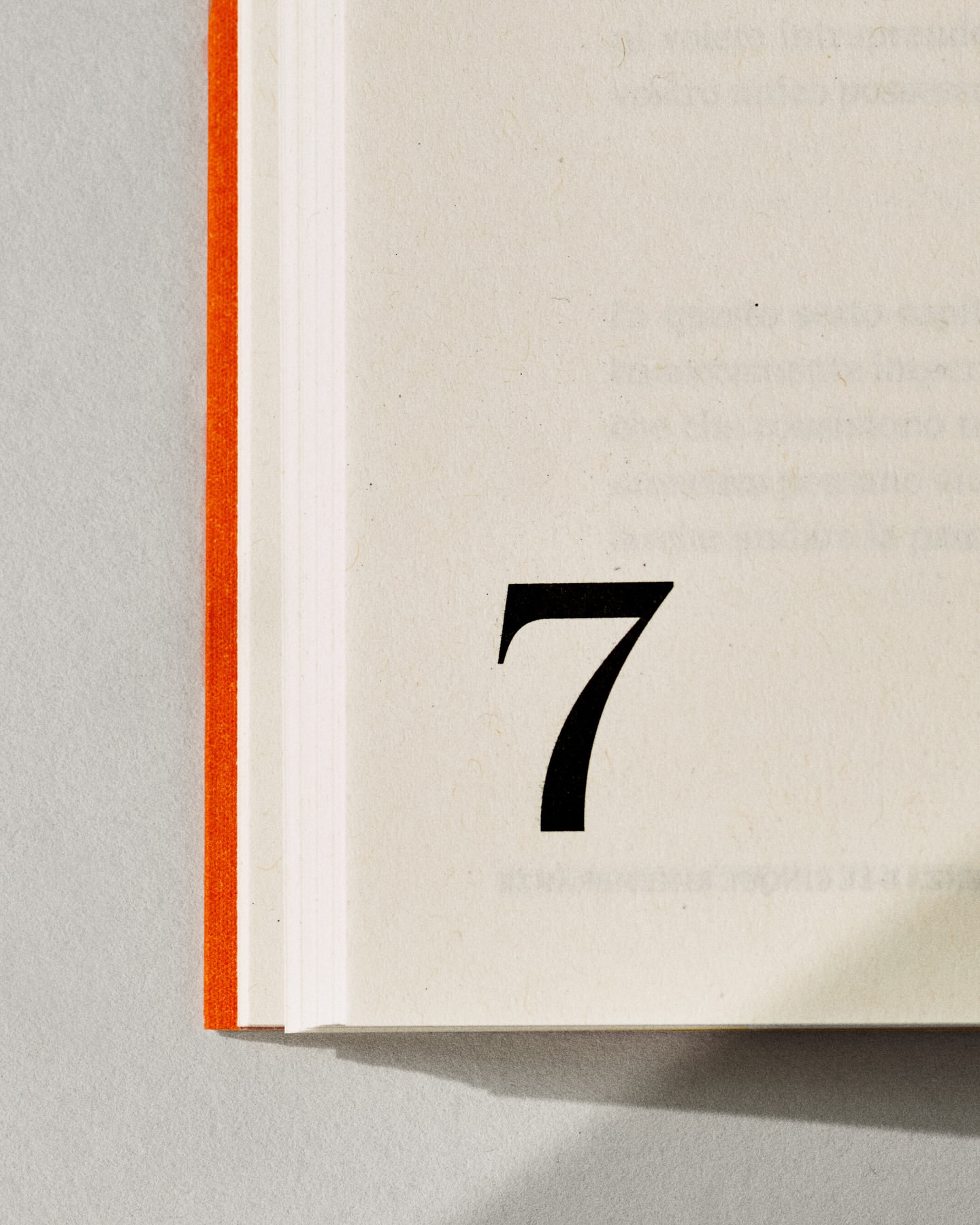 Close-up of open book with the number seven printed in black on the right page, binding visible on the left side of the frame.