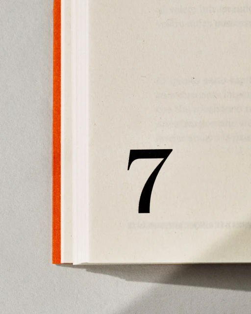 Close-up of open book with the number seven printed in black on the right page, binding visible on the left side of the frame.