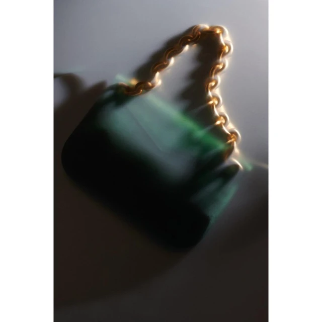 Green satin purse with gold chain detail on a blurred background, fashionable and elegant accessory, studio shot for product display.