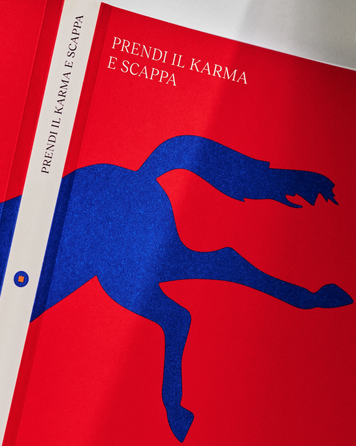 Book covers on display featuring a red backdrop and a blue silhouette figure, with Italian text 'PRENDI IL KARMA E SCAPPA'.