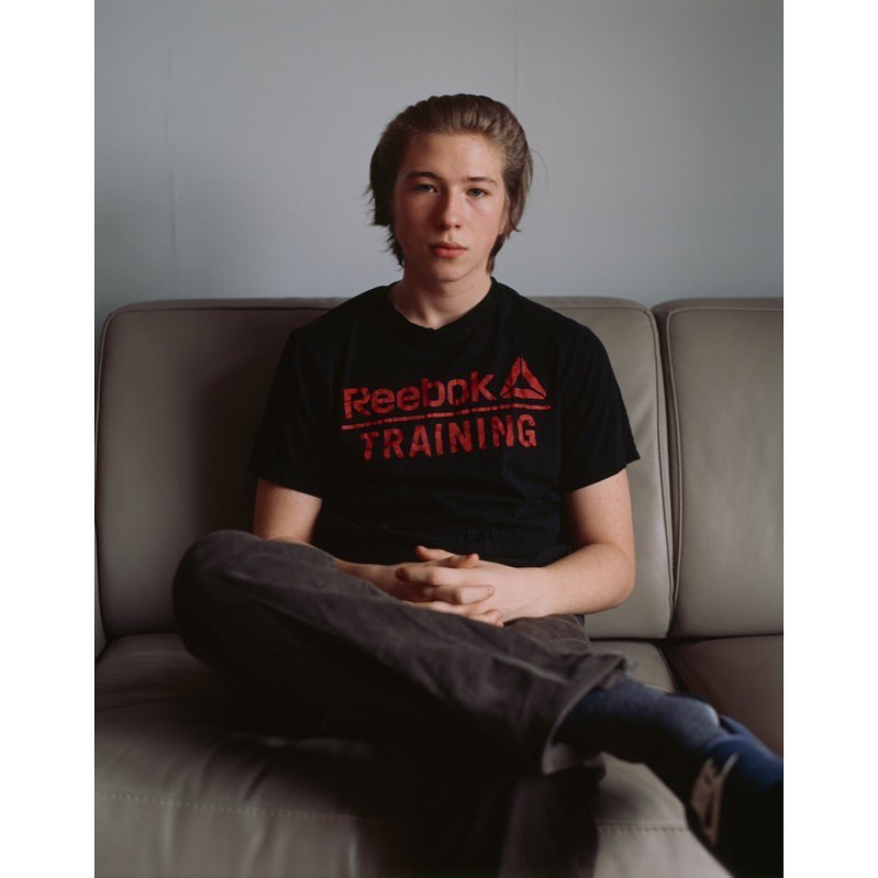 Adult seated on couch with Reebok Training t-shirt, shot indoors with a shallow depth of field, lit naturally for a relaxed portrait.