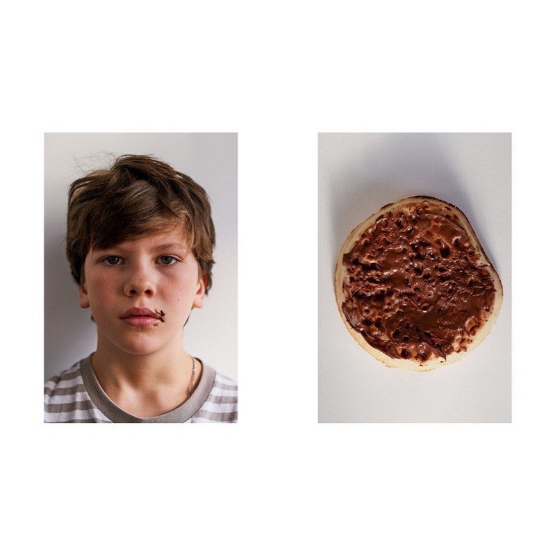 A young person with brown hair is seen with chocolate around their mouth, next to a pancake covered in chocolate spread on a white background.