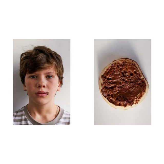 A young person with brown hair is seen with chocolate around their mouth, next to a pancake covered in chocolate spread on a white background.