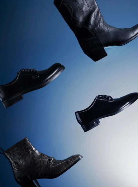 Studio shot displaying an array of mens' footwear, including dress shoes and ankle boots, against a gradient blue background.