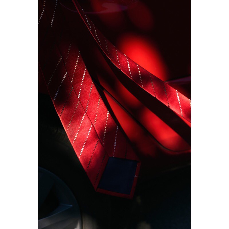 Red tie with striped pattern in dappled sunlight, showcasing men's fashion accessory with elegant design and bright, contrasting lighting.