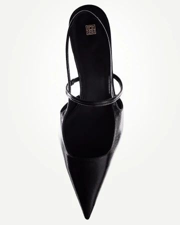 High angle studio shot of a single black leather pointed-toe slingback heel against a white background, showing the shoe's shape and straps.