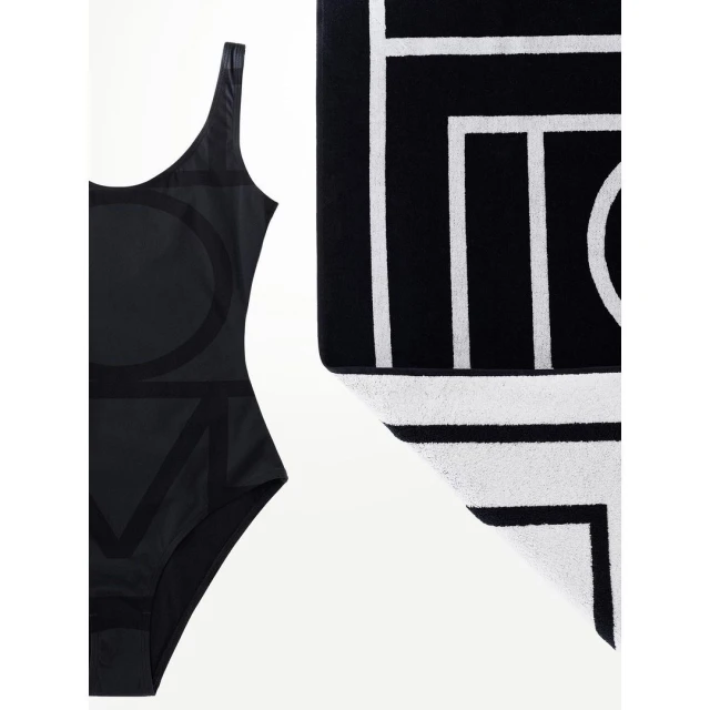 Black one-piece swimsuit with oversized LOVE text and a black and white geometric towel on a white background. Minimalist swim fashion.