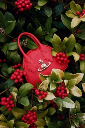 Red heart-shaped handbag nestled among green leaves and clusters of bright red berries