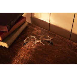 Wire-rimmed glasses resting on a dark wooden desk next to a stack of antique hardcover books.