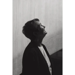 Monochrome portrait of an elderly woman looking upward with a slight smile against a textured concrete wall