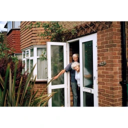 Elderly couple standing in the open doorway of a brick residential building, photographed by Tex Bishop.