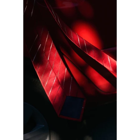Close-up studio photograph of a vibrant red silk necktie featuring diagonal pinstripe patterns, captured in dramatic low-key lighting.