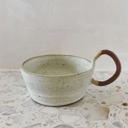 Ceramic handled cup with speckled glaze resting on a patterned terrazzo surface against a neutral wall