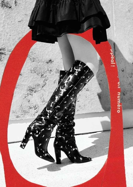 Fashionable black and white pattern knee-high heeled boots with a black ruffle mini skirt, set against a textured backdrop with red circle.