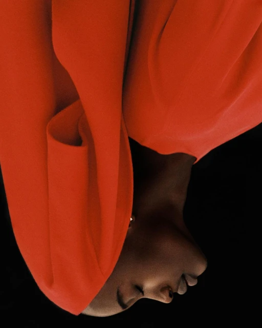 Close-up portrait of a Black woman with a closed-eyes expression, wearing a vibrant red dress against a stark black backdrop.