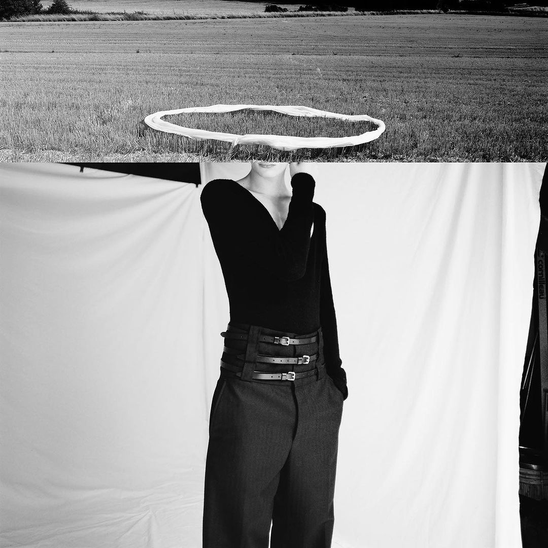 Artistic black and white fashion photo featuring a model in high-waisted belted pants against a studio backdrop with a field landscape on top.