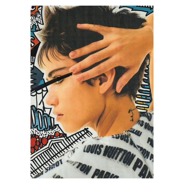 Close-up of a woman with short hair applying mascara against a colorful graphic art background with fashion brand text.