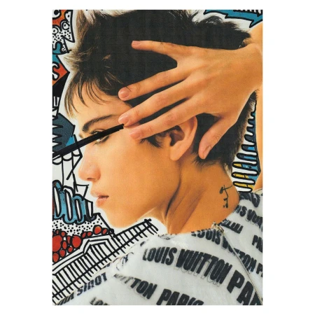 Close-up of a woman with short hair applying mascara against a colorful graphic art background with fashion brand text.