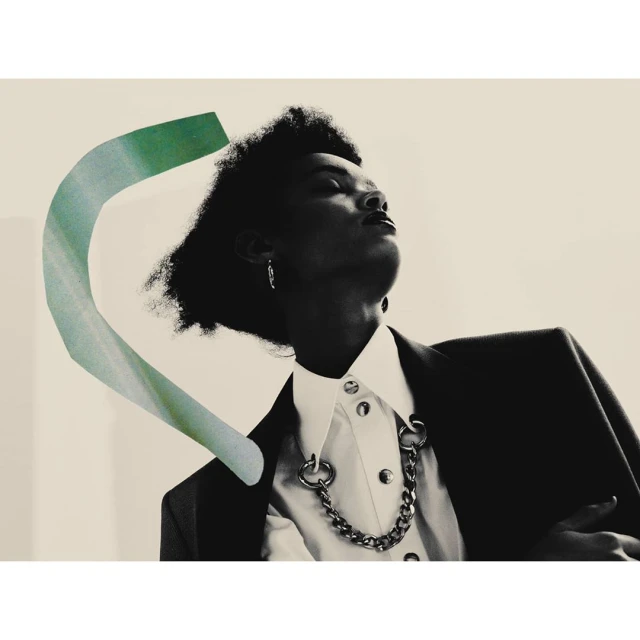 Fashion shot featuring a black adult woman in a white button-down shirt and dark blazer with a green curved shape overlay.