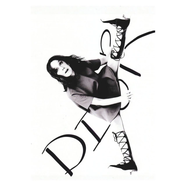 A woman with dark hair and a dress, performs a leg split in lace-up boots, posing against a white background with large black handwritten text.