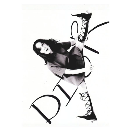 A woman with dark hair and a dress, performs a leg split in lace-up boots, posing against a white background with large black handwritten text.