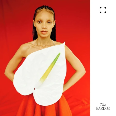 Model with braided hair holding a large white anthurium leaf in front of her chest against a red background.
