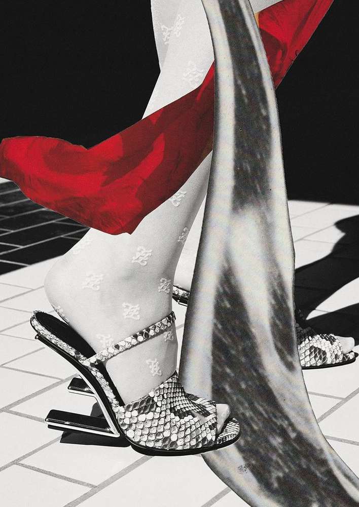 Fashion editorial shot of woman's legs in patterned stockings and high-heel sandals, accented by red fabric and grey sculpture on tile.