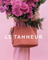 Person holding a large bouquet of bright pink flowers and a structured rust orange handbag against a solid pink background.