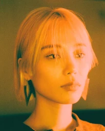 Portrait of a woman with blonde hair and geometric earrings under warm orange lighting in Paris by The Bardos