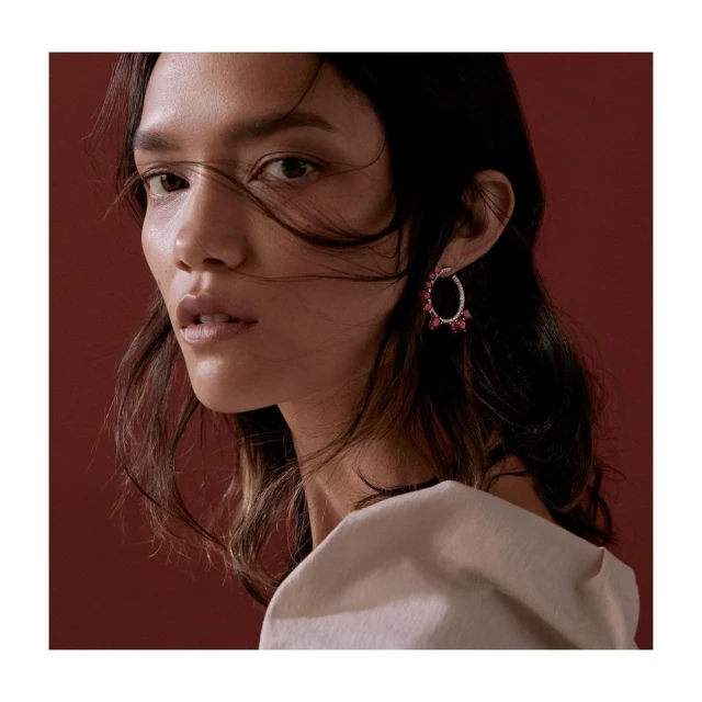 Portrait of a fashionable woman with an elegant earring, against a solid red background in a studio setting, for beauty or jewelry concepts.