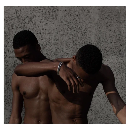 Two shirtless Black men posing together against a textured concrete wall, photographed in London by The Masons.