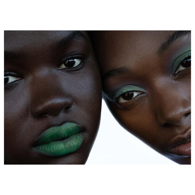 Close-up portrait of two dark-skinned adult women with green makeup on a white background, showcasing beauty and makeup artistry.