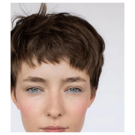 Close-up portrait of a young adult female with short brown hair and blue eyeliner on a white background, showcasing beauty and makeup.