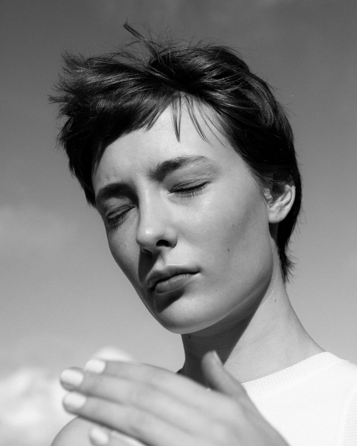 Black and white close-up portrait of a fair-skinned adult female with short hair and closed eyes in an outdoor setting with sunlight.