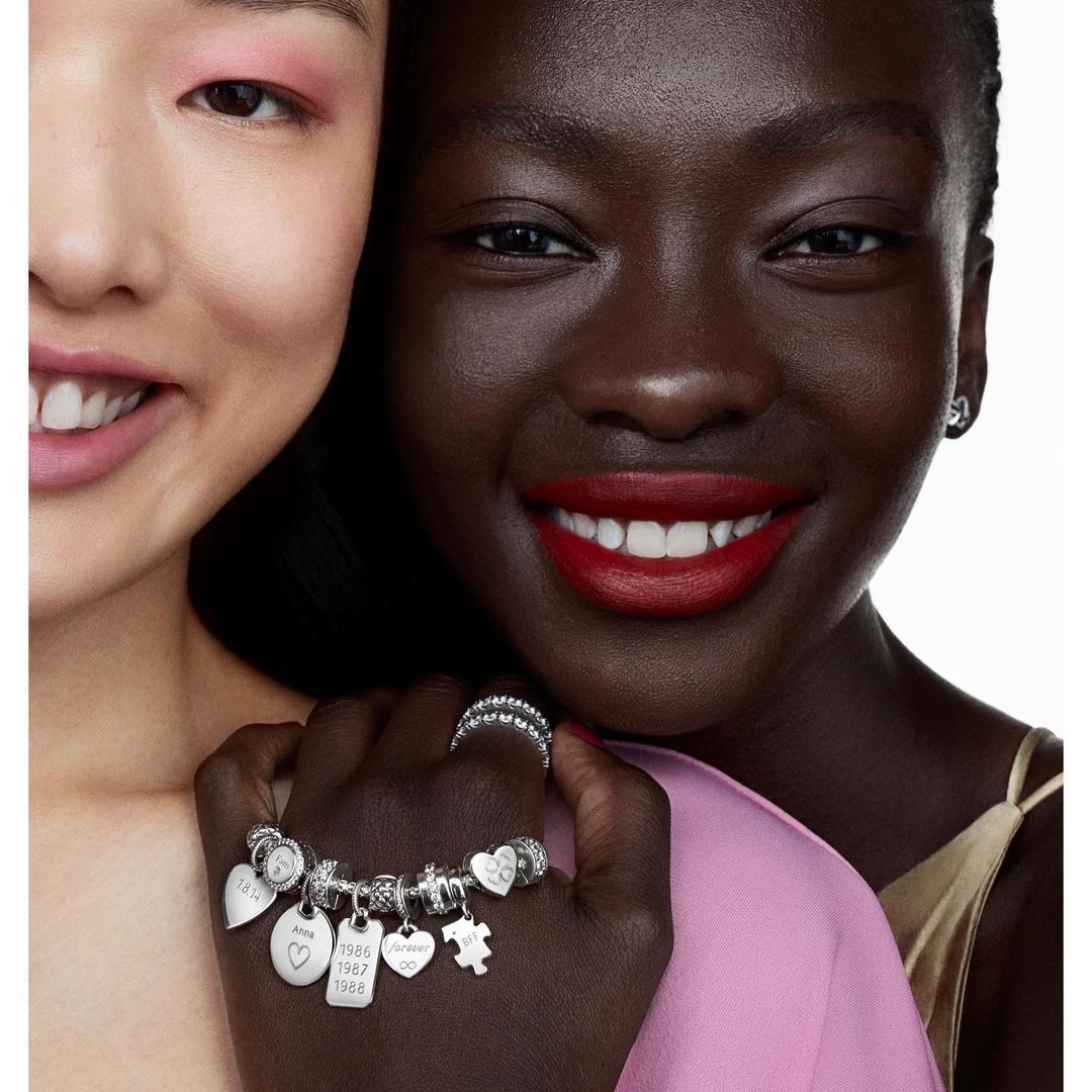 Close-up of two smiling women of different ethnicities showcasing a charm bracelet, highlighting diversity and jewelry.