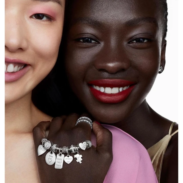 Close-up of two smiling women of different ethnicities showcasing a charm bracelet, highlighting diversity and jewelry.