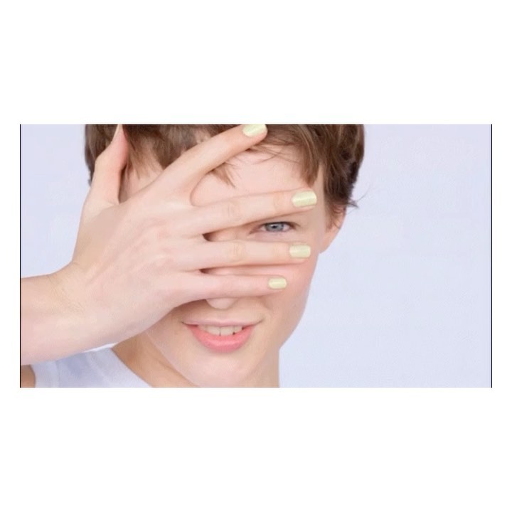 Close-up portrait of a smiling young adult female with short hair and manicured nails, partially covering her face with her hand.