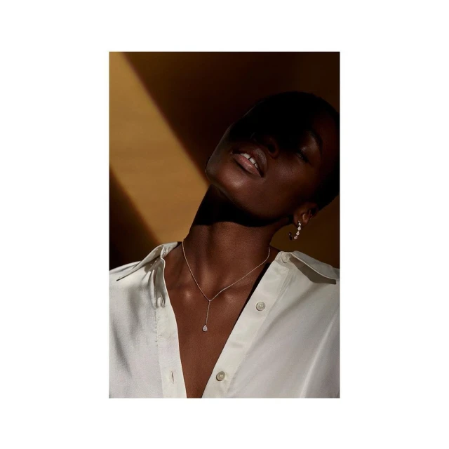 Close-up of a Black female model wearing a light-colored blouse and a gold necklace, with a sunlit yellow background creating shadows.