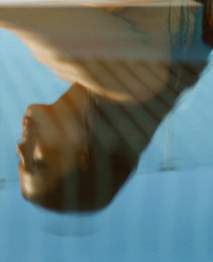 Abstract portrait of an adult female, shot from a low angle, featuring soft lighting and a blue background, blurred for a dreamlike effect.