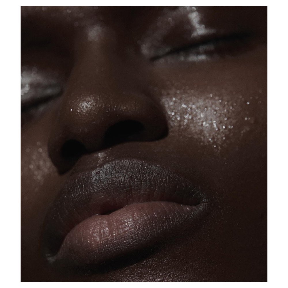 Close-up portrait of a Black woman with closed eyes, showcasing glistening skin with a radiant glow and accentuated features.