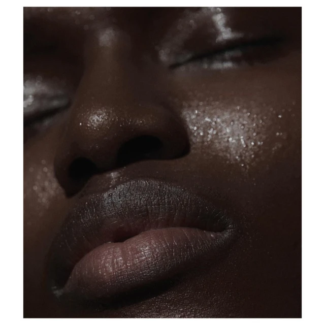 Close-up portrait of a Black woman with closed eyes, showcasing glistening skin with a radiant glow and accentuated features.