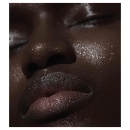 Close-up portrait of a Black woman with closed eyes, showcasing glistening skin with a radiant glow and accentuated features.