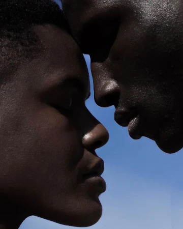 Close-up portrait of two Black men facing each other against a bright blue sky background.